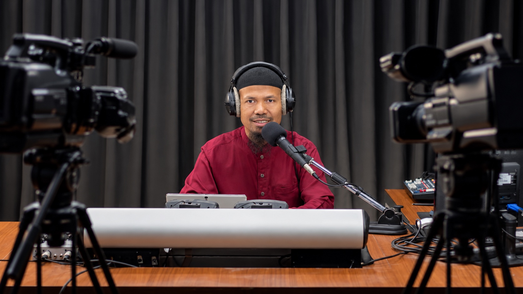 Pemateri berbicara di studio Radio Hang dengan mikrofon dan kamera; foto dokumentasi yang disunting secara digital.
